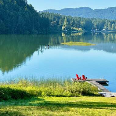 dock with red adiriondack chairs and a man in a rowboat in the distance 